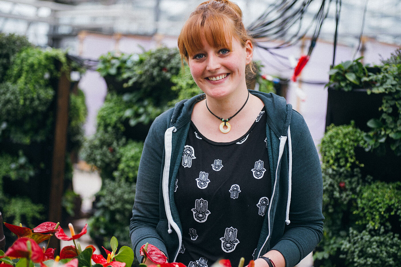 Eine junge Frau steht in einem Gewächshaus, im Hintergrund sind mobile begrünte Wände, im Vordergrund rot blühende Pflanzen. © Hessen schafft Wissen – Steffen Böttcher