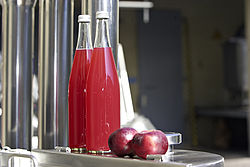 roter Saft in Glasflaschen mit Frucht nebendran liegend 