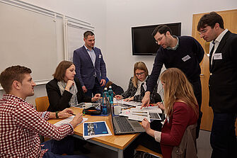 Drei Herren in Anzügen und Hemd erklären einer Gruppe Studierender anhand von Abbildungen und Texten etwas. © Hochschule Geisenheim / Winfried Schönbach