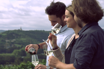 Drei junge Menschen stehen vor einem Weinbergspanorama und trinken Wein. © Hochschschule Geisenheim